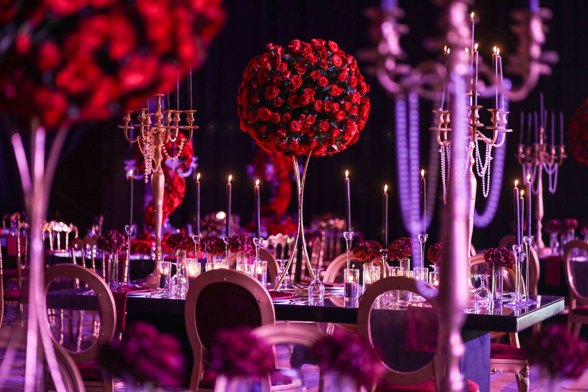 Beautiful bouquet of red roses on a wedding table surrounded by glowing candles.